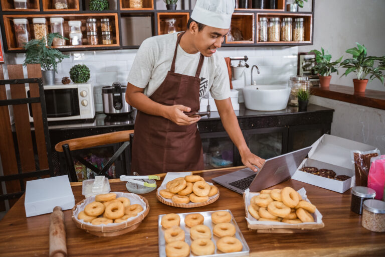 a professional male chef with a mobile phone prepares a donut order holding a digital tablet to