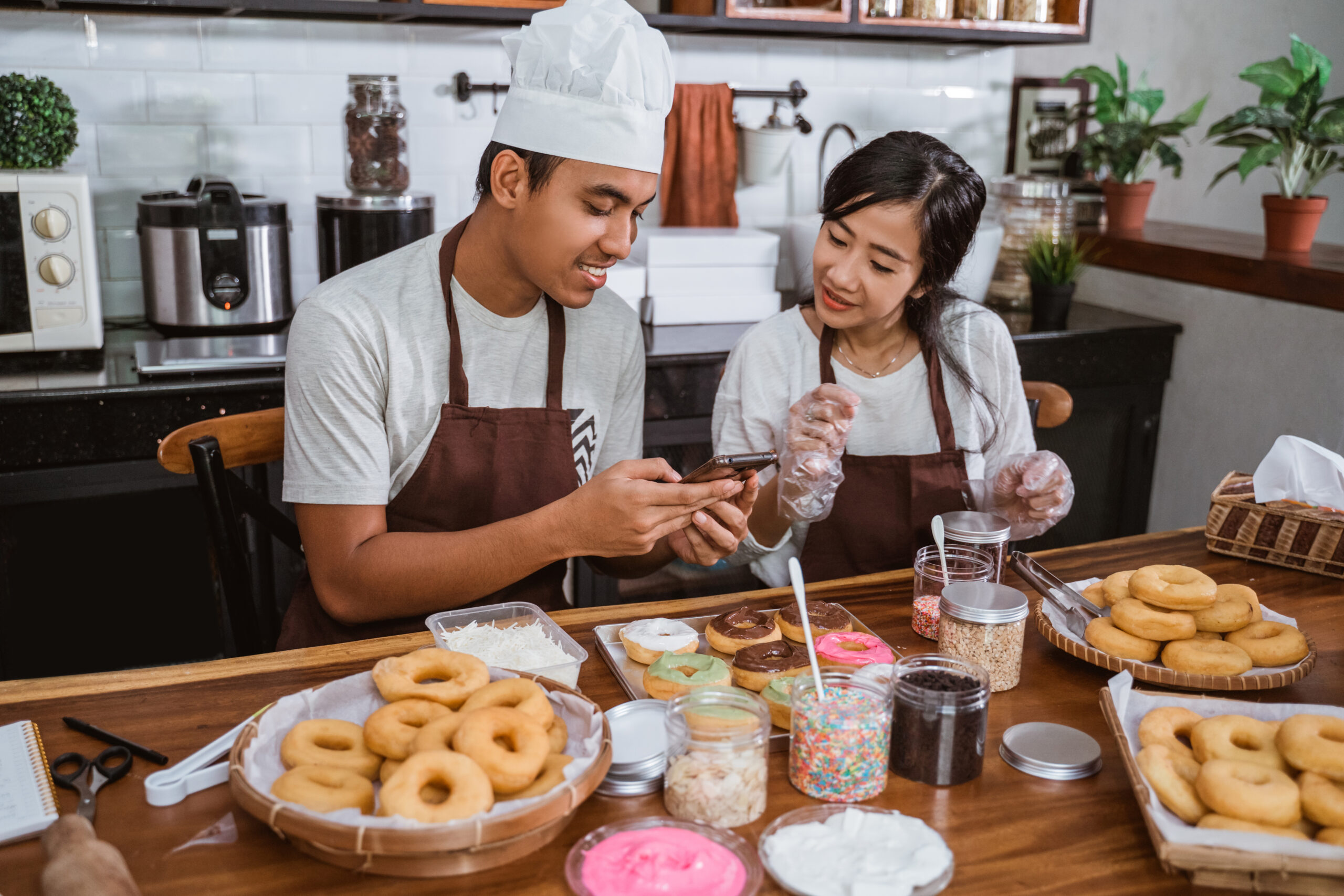 chefs wearing aprons use their cell phones to sell online after making donuts together